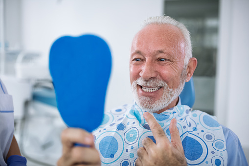 male patient holding up a mirror and checking his smile for receding gums