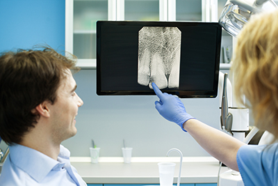 patient sitting in a dental chair reviewing an x ray image with his dentist