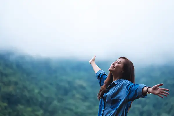 Smiling woman with arms outstretched in nature, breathing with her mouth closed.